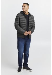 Jachetă puffer neagră cu design matlasat orizontal, închidere cu fermoar și glugă, asortată cu blugi negri și adidași negri. Tricou simplu negru dedesubt.