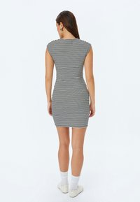 Sort-og-hvid stribet bodycon-kjole med korte ærmer, tætsiddende form og knælang længde, parret med hvide sokker og hvide sko.