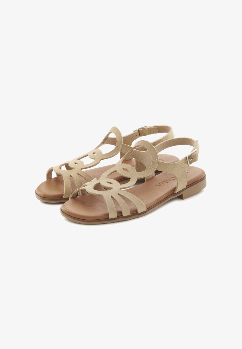 Beige suede sandals with cut-out design and a back strap. Flat sole with a light brown insole, featuring decorative loops and soft texture.