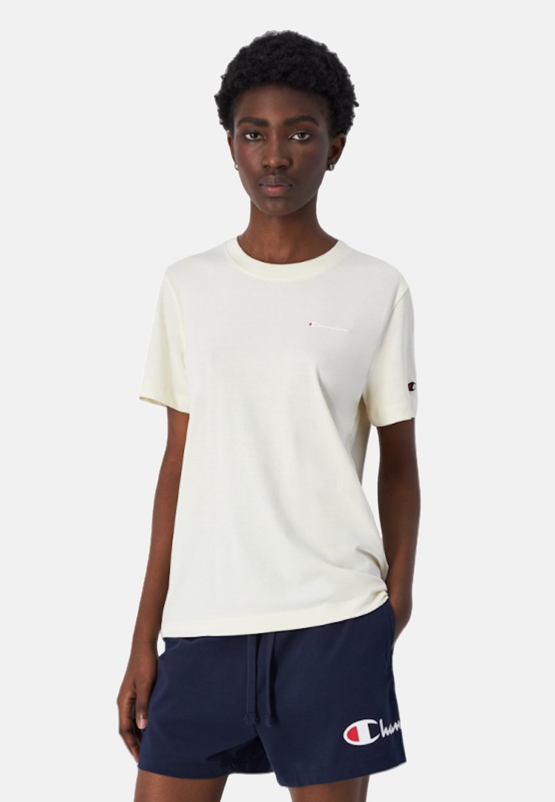 Camiseta de algodón crema con mangas cortas y cuello redondo, con un pequeño logo rojo y blanco en el pecho. Pantalones cortos azul marino con un detalle de logo.