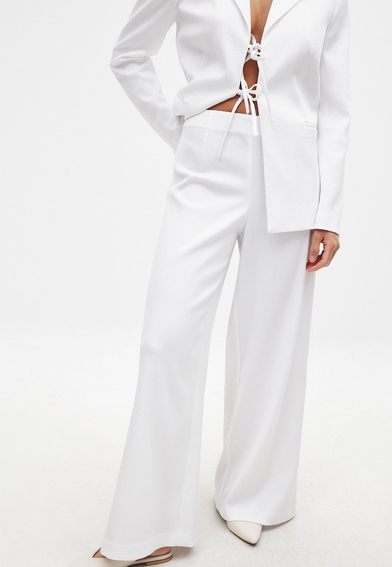 Valge bleiser ja laiad püksid, millel on tekstuuriga viimistlus. Bleiseril on ees side ja veidi üle mõõtude klapid.