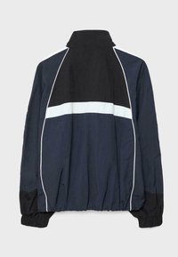 Mørkeblå og sort vindtæt jakke med hvid vandret stribe og kantning, elastiske manchetter og høj krave, vist bagfra.