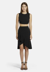 Zwarte cropped top met een ronde hals, gecombineerd met een zwarte rok tot de knie met een diagonale ruffle en een asymmetrische zoom.
