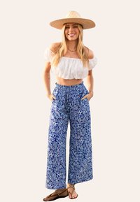 Witte off-the-shoulder crop top, blauwe wijde geprinte broek en een rieten hoed; heeft een ontspannen pasvorm, bloemenprint en zakken.