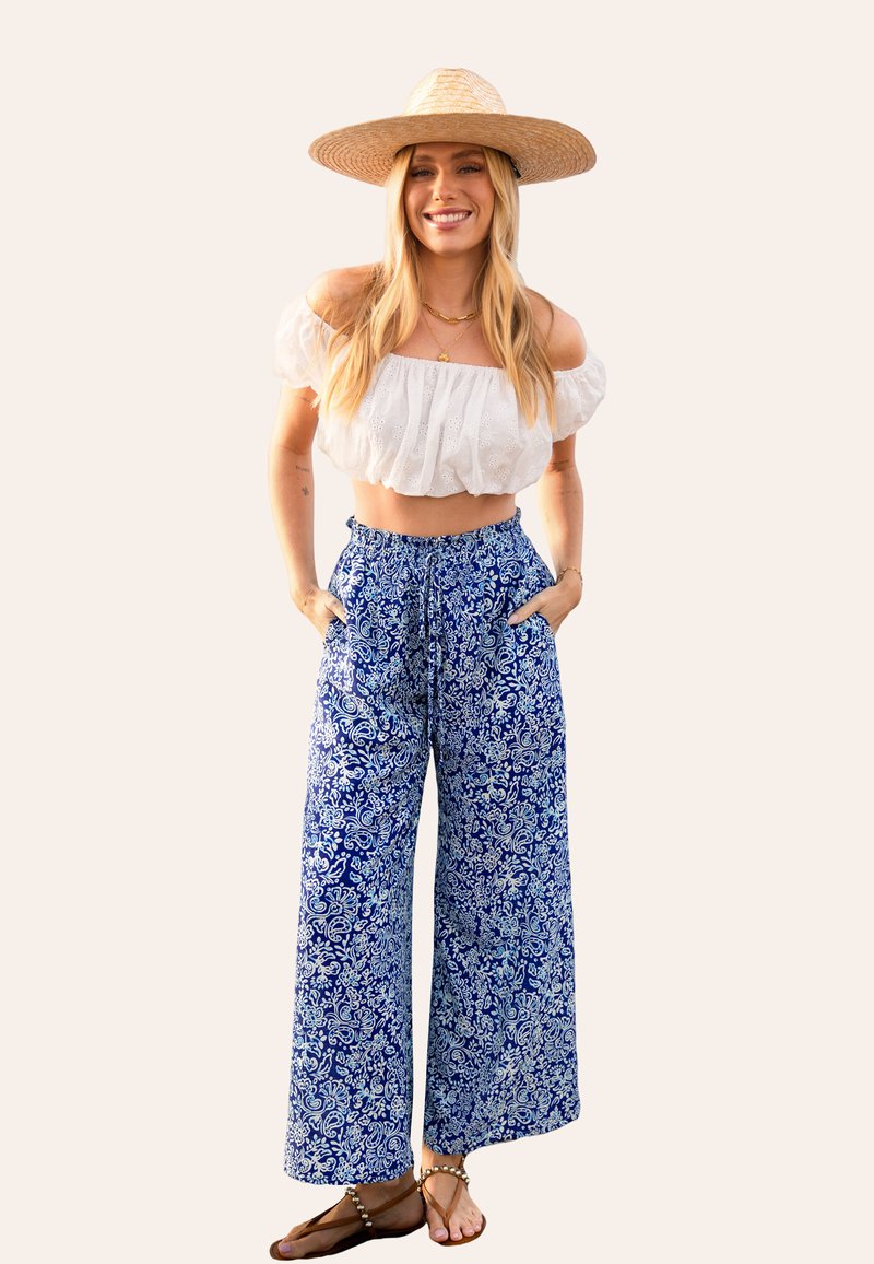 Witte off-the-shoulder crop top, blauwe wijde geprinte broek en een rieten hoed; heeft een ontspannen pasvorm, bloemenprint en zakken.