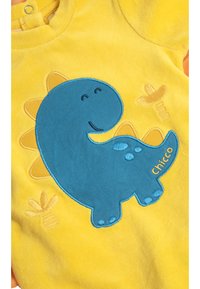 Body de bebé amarillo con bordado de un dinosaurio azul, que presenta ojos sonrientes y detalles en forma de gota de agua. Incluye el nombre de la marca "Chicco".
