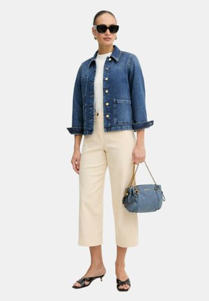 Ženska, ki nosi temno modro denim jakno čez bel top, krem hlače z širokimi hlačnicami, črne sandale s peto, črna sončna očala in drži modro torbico.