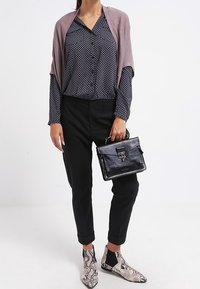 Schwarze Hose, gemusterte marineblaue Bluse, hellmauvefarbener Schal, schwarze Handtasche und beige- und schwarze Schlangenleder-Stiefeletten.