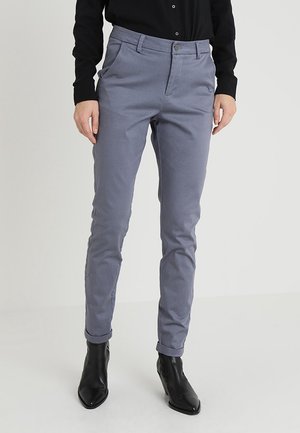 Lichtgrijze, op maat gemaakte broek met een slim fit, voorzien van een gladde textuur, riemlussen en opgerolde zoom, gecombineerd met zwarte enkellaarsjes.