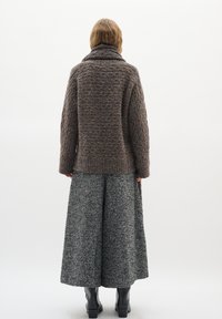 Brauner, strukturierten Wollpullover mit weitem Kragen, kombiniert mit einem grauen Hahnentritt-Rock, schwarze Knöchelstiefel sind am unteren Ende sichtbar.
