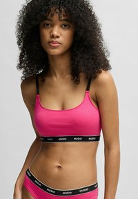 Rosa bomulls-bralette med svarta justerbara band och en bred svart remsa med "HUGO"-logotypen. Slät textur, enkel design och figurnära passform.