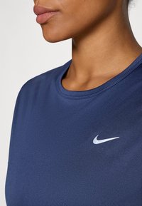 Granatowa, krótko rękawowa koszulka sportowa z okrągłym dekoltem, wykonana z gładkiej tkaniny. Posiada małe, białe logo Nike na lewej piersi.