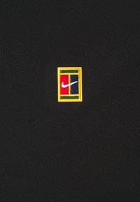 Tissu noir présentant un logo carré brodé avec une bordure jaune. Le logo comprend des sections rouges, bleues et vertes avec un swoosh blanc.