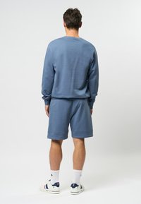 Lichtblauwe sweatshirt en bijpassende shorts, van katoen, met een relaxte pasvorm, effen textuur, gedragen met witte sokken en casual schoeisel.