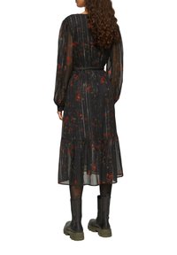 Schwarz floral midi Kleid mit langen, transparenten Ärmeln, tailliertem Schnitt und gerafftem Saum, kombiniert mit klobigen schwarzen Stiefeln.