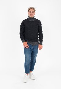 Czarny sweter z golfem, wykonany z teksturowanej tkaniny z szarymi akcentami, zestawiony z jasnoniebieskimi dżinsami i białymi trampkami. Poza stojąca na białym tle.