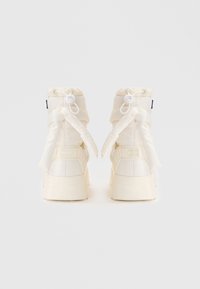 Baskets plateformes blanches avec un haut rembourré, fermeture à lien de serrage et accents en ruban. Texture lisse avec un léger éclat, design minimaliste.