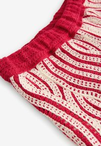 Couverture au crochet avec un design rouge et crème, présentant des rayures alternées et des motifs complexes, mettant en valeur une apparence texturée et tissée.