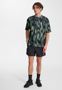 Grafisk svart och grön tie-dye t-shirt med korta ärmar, rund halsringning och en liten logotyp på bröstet, ihop med svarta shorts och strumpor.