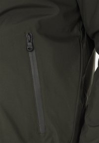 Giacca verde oliva scura caratterizzata da una tasca con zip sul lato sinistro, realizzata in materiale liscio e resistente all'acqua con una finitura opaca.