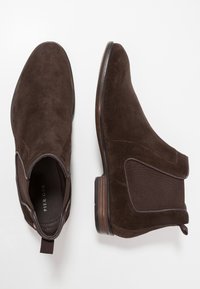 Bottines en daim marron avec panneaux latéraux élastiques, bout arrondi et talon bas empilé. Dotées d'une languette pour un enfilage facile.