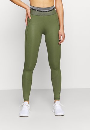 Olivgröna leggings med hög midja i svart och vitt randigt mönster. Tillverkade av elastiskt material, med en slät yta och sidofickor.