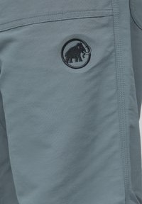 Close-up of gray fabric with a black embroidered mammoth logo inside a circle near stitched seams.