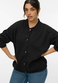Giacca nera imbottita con collo rotondo, bottoni a pressione sul davanti e polsini elasticizzati. Presenta un design testurizzato e una vestibilità rilassata.