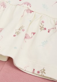 Light cream fabric with pink flamingo and floral prints, featuring a gathered ruffle at the hem, over a soft pink ribbed fabric.