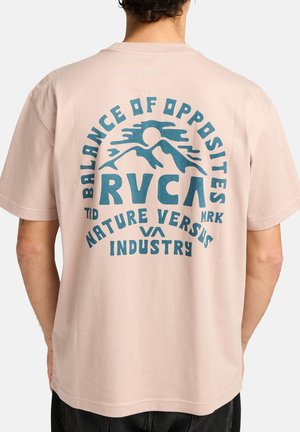 T-shirt en coton rose avec un graphique audacieux en bleu représentant des montagnes et un soleil, texte indiquant "Équilibre des Opposés" et coupe décontractée.