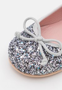 Ballet flat argentato glitterato con superficie testurizzata, caratterizzato da un dettaglio a fiocco grigio e una morbida fodera interna rosa. Punta rotonda e suola piatta.