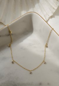 Collana in oro con quattro piccoli accenti in cristallo, collegamenti delicati e un design minimalista, posata su un piatto in marmo bianco.