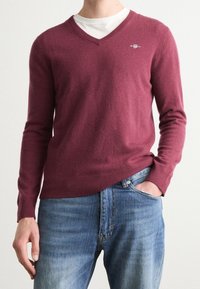 Pull col en V bordeaux en matière douce, avec manches longues et ourlet côtelé, associé à un jean en denim bleu clair.