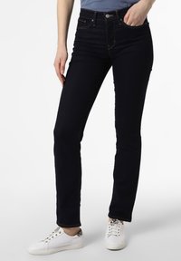 Jeans skinny azul oscuro de mezclilla con costuras amarillas en contraste, una cintura de altura media y bolsillos frontales, combinados con zapatillas blancas.