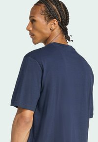 Námornícky modré bavlnené tričko s kulatým výstrihom, krátkymi rukávmi a voľným strihom. Obsahuje prešívanie na výstrihu a ramenách.