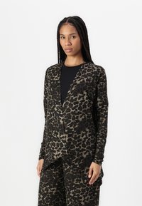 Svart och tan djurtryck cardigan med långa ärmar, avslappnad passform och draperad frontdesign, parat med en svart skjorta under.