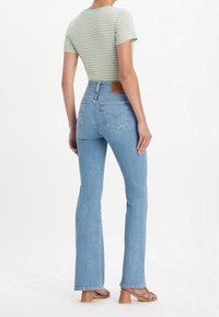 Jean bleu clair taille haute avec jambe évasée, tissu en denim, et coutures distinctives sur les poches arrière. Associé à un t-shirt rayé vert.