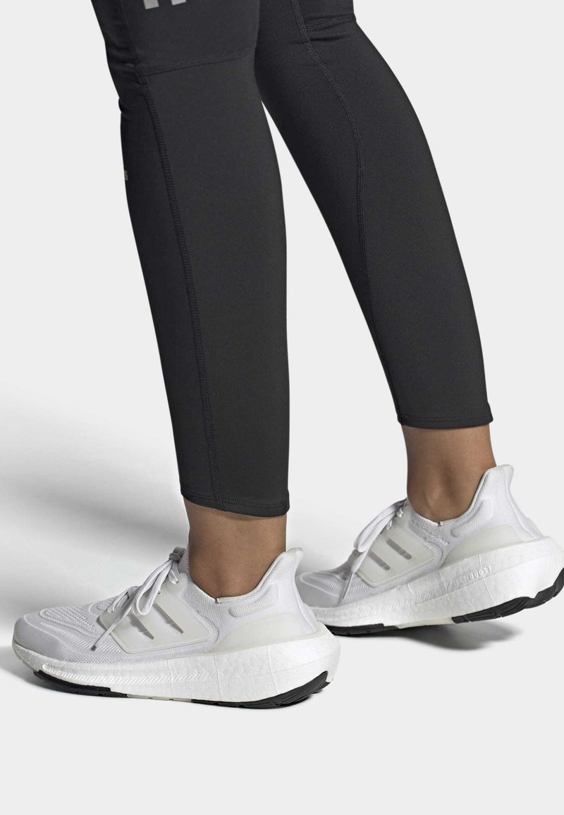 Witte sportieve schoenen met bovenwerk van mesh, drie zijstrepen en een gestructureerde zool; gecombineerd met zwarte strakke leggings.
