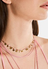 Chokerhalsband med rosa snören, guldaccenter och små pärldetaljer, med dekorativa guldskivor som är jämnt fördelade längs designen.