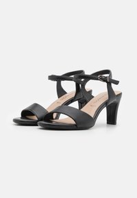 Black leather open-toe heeled sandals with cross straps and an adjustable ankle buckle. Features a smooth texture and a tapered heel.