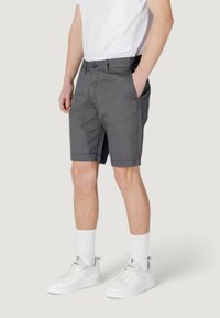 Pantaloni corti grigi a fantasia con fronte piatto, tasche laterali e chiusura a bottone, indossati con sneaker bianche e calze lunghe fino al polpaccio.