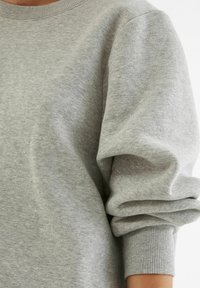 Harmaa sweatshirt, jossa on pyöreä kaula-aukko, ribbireunat ja tilavat hihat. Valmistettu pehmeästä, teksturoidusta kankaasta, jossa on hienovarainen kuvio.