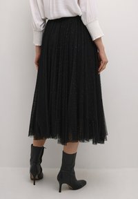 Black tulle midi skirt with pleats, featuring a decorative pattern. Paired with fitted black ankle boots with a pointed toe and stiletto heel.