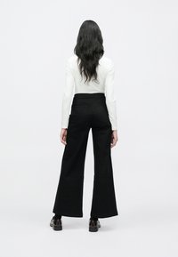 Pantaloni negri cu croială largă și talie înaltă, realizați din denim. Au buzunare în spate și un design curat, minimalist. Textura este netedă și durabilă.