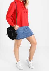 Felpa rossa con cappuccio, gonna di jeans, sneakers bianche e una borsa a tracolla nera. Il tessuto è morbido e il design è casual e aderente.