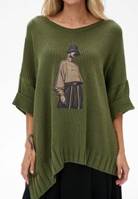 Oliwkowy sweter z dzianiny z oversize'owymi rękawami, z graficznym nadrukiem modelki w paskowanym ubiorze z przodu. Ribbowany detal u dołu.