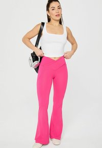 Fitted white ribbed tank top paired with pink flared yoga pants featuring a crossover waistband. Accessories include a black bag and headphones.