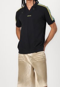 Czarna koszulka polo z zielonymi, żółtymi i białymi paskami na rękawach. Posiada dekolt w serek oraz haftowane logo na piersi.