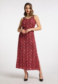 Robe maxi à imprimé serpent rouge avec des fines bretelles, un corsage ajusté et une fente sur le côté, assortie à des talons hauts noirs. Tissu à texture lisse.