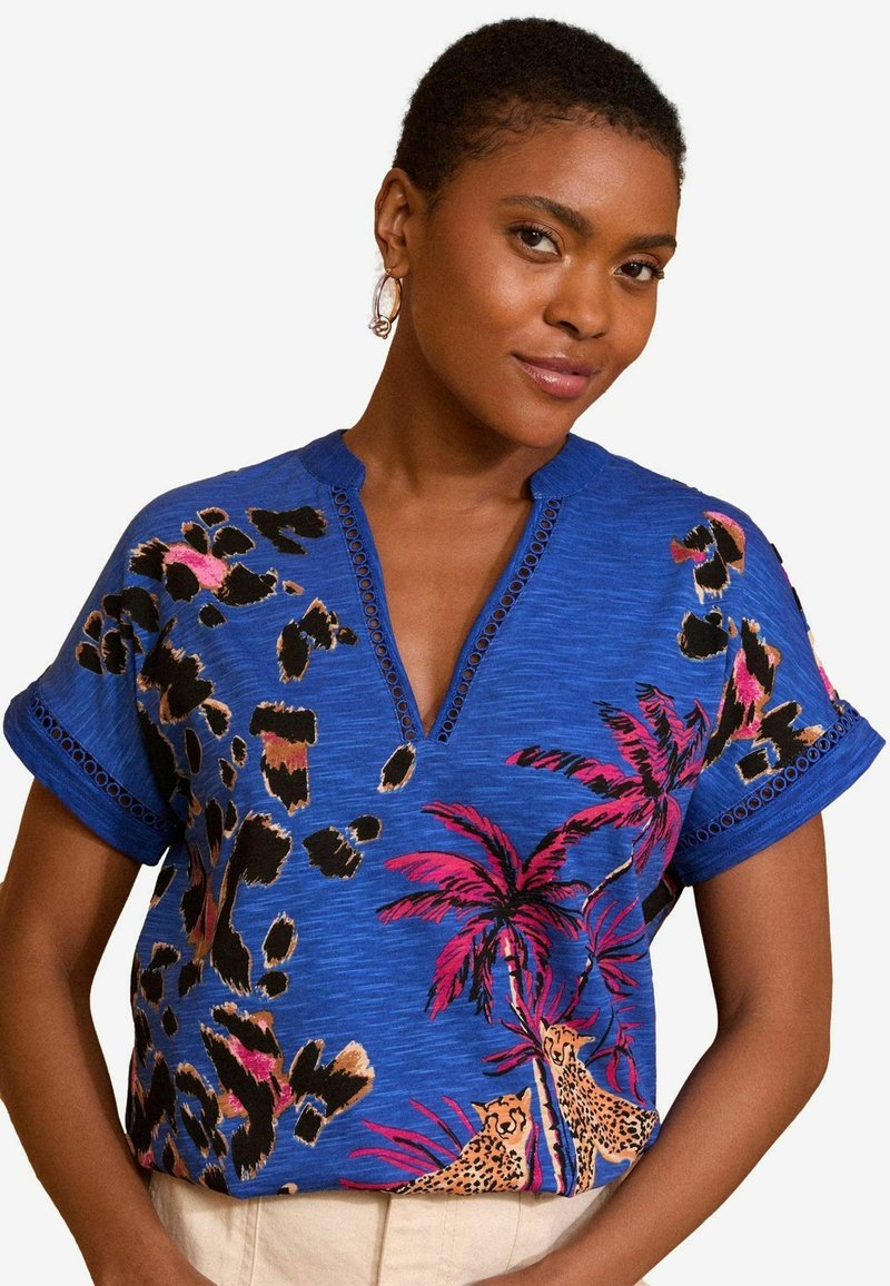 Rövid ujjú kék blúz leopárd- és pálmafalevelet mintázó dizájnnal, V-kivágással és díszített kivágásokkal az ujjak mentén.